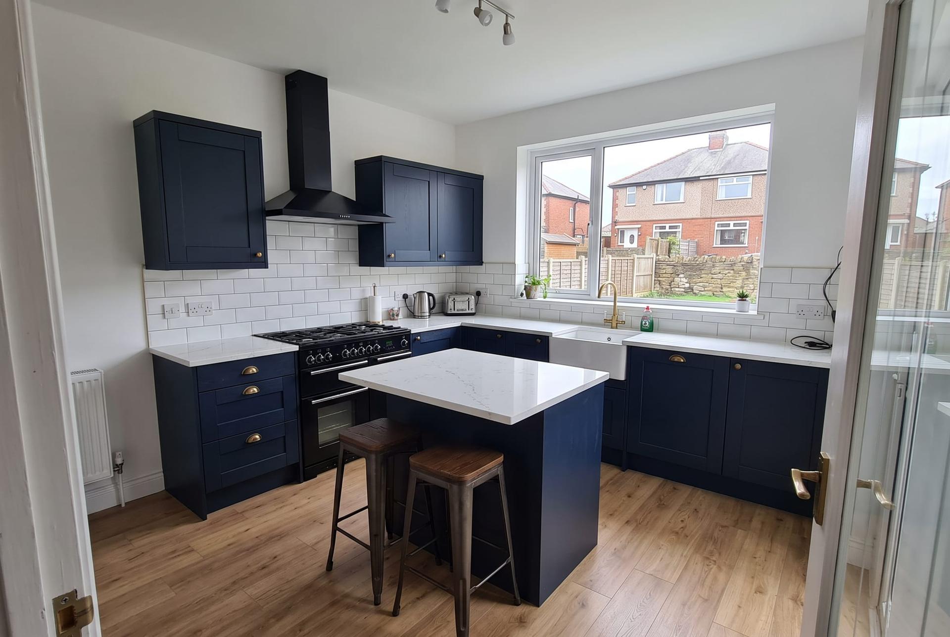 A navy shaker kitchen with a small island and a window to the garden