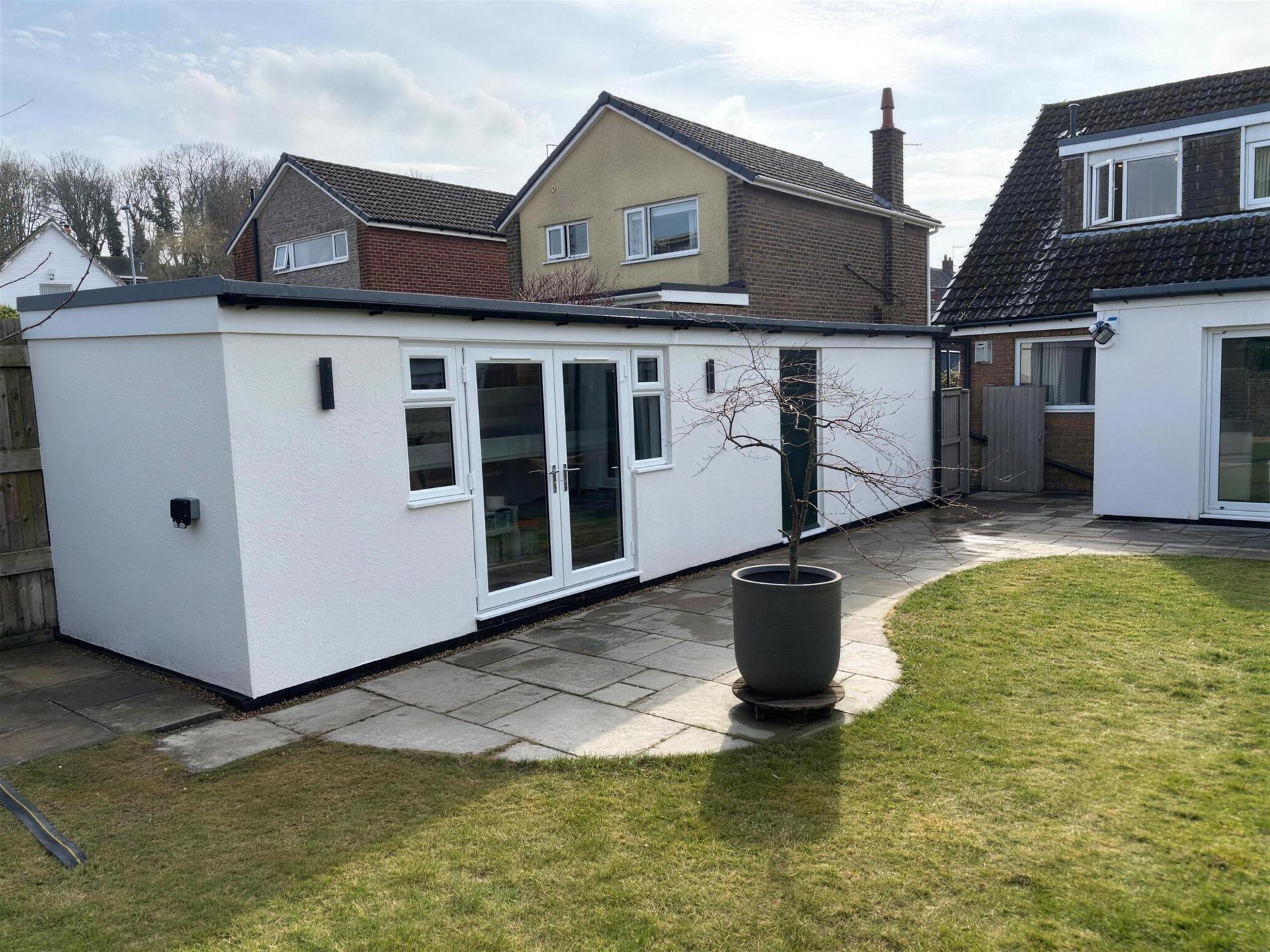The finished garage office from the garden, white render and French doors